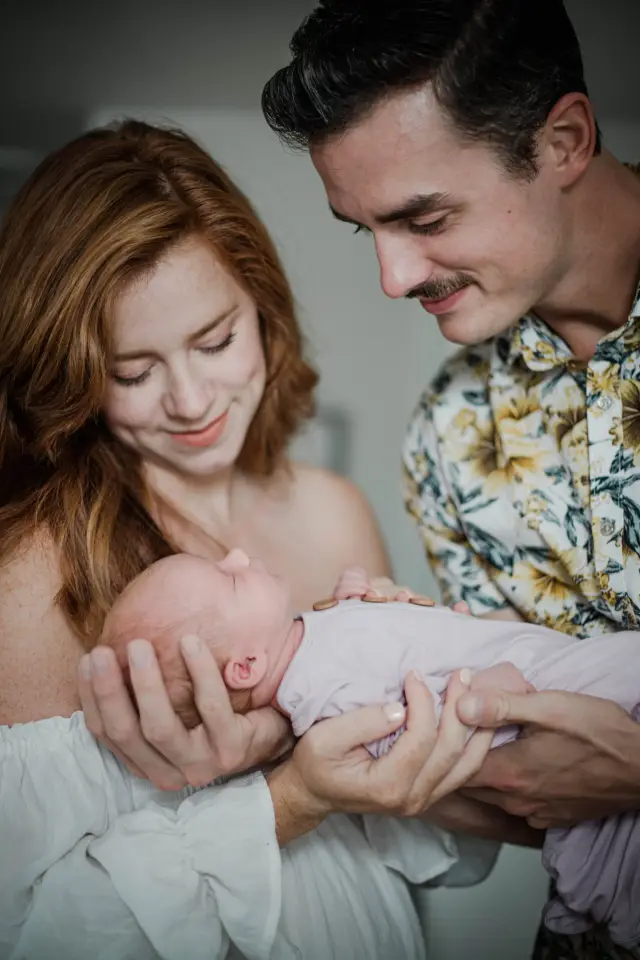 Parents cradling their newborn and smiling down at her