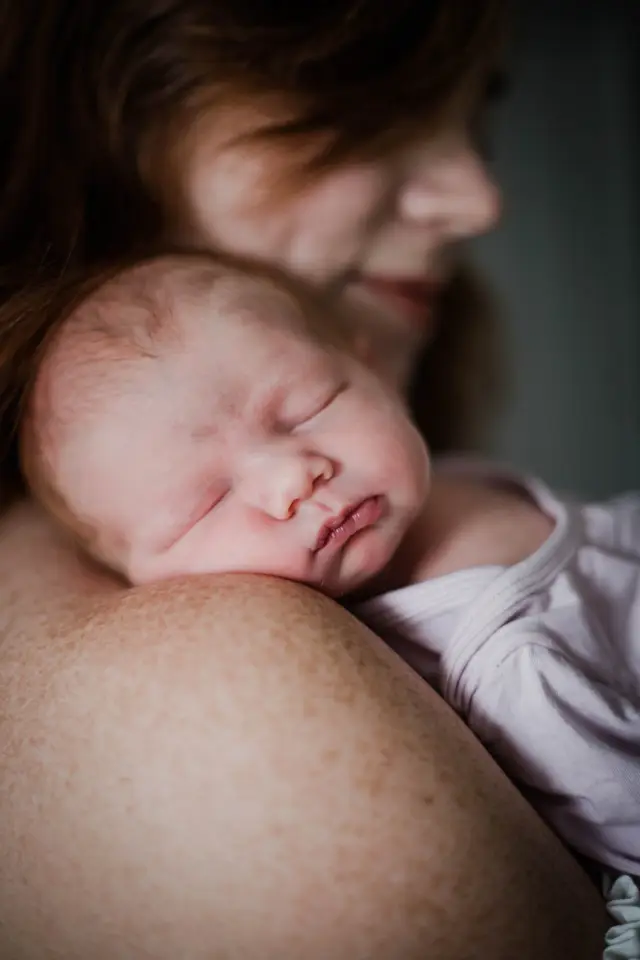 Sleeping newborn resting on mom's shoulder in soft window light