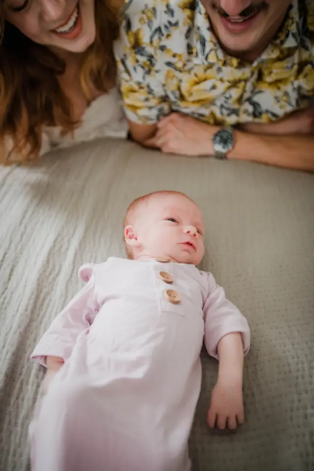 Parents leaning over their newborn lying on the bed in a pink sleeper