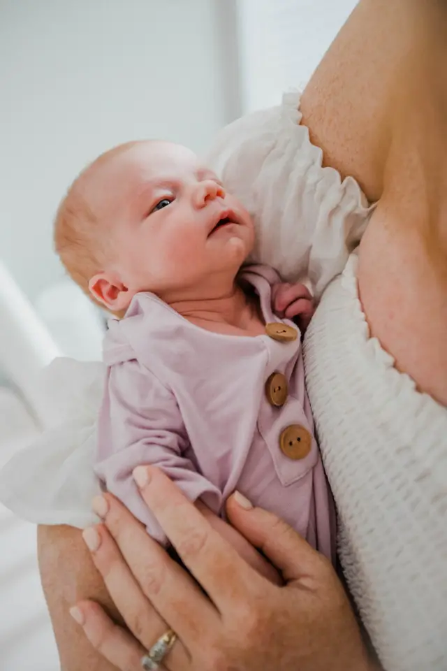 Newborn in a pink button sleeper looking up from mom's arms