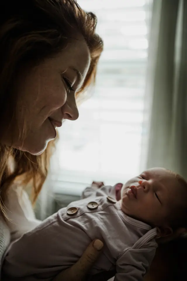 Mom smiling down at her newborn in the light from the window