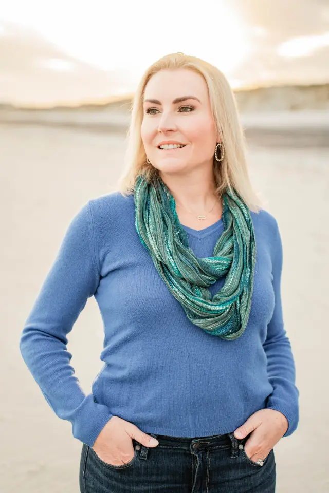 Woman in a blue sweater and green scarf smiling on the beach