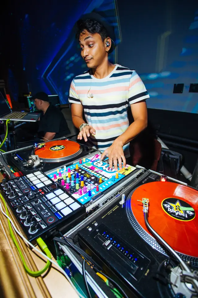 DJ working the turntables with orange vinyl and a controller