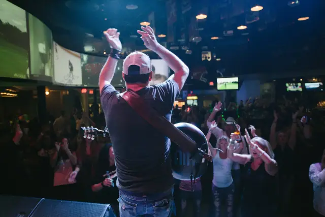 Performer on stage raising his arms to a packed crowd