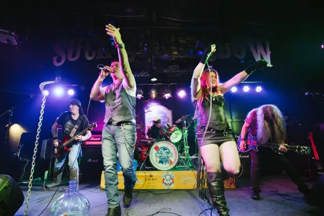 Rock band performing on a club stage with the singers' arms raised