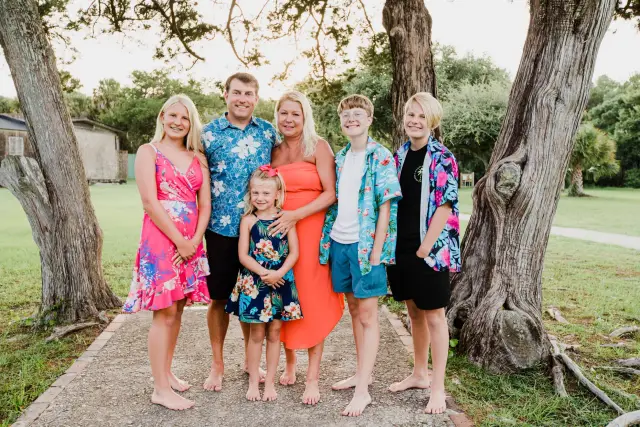 Big family in bright tropical prints posing barefoot under live oaks
