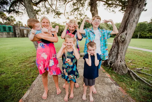 Family in tropical prints making silly faces and heart hands under the oaks