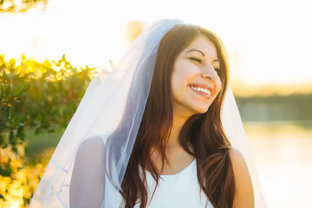 Bride in a long veil smiling at sunset with golden light behind her