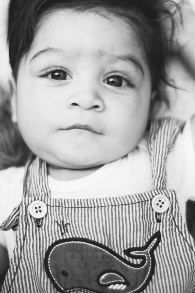 Black and white portrait of a baby in striped overalls with a whale on them