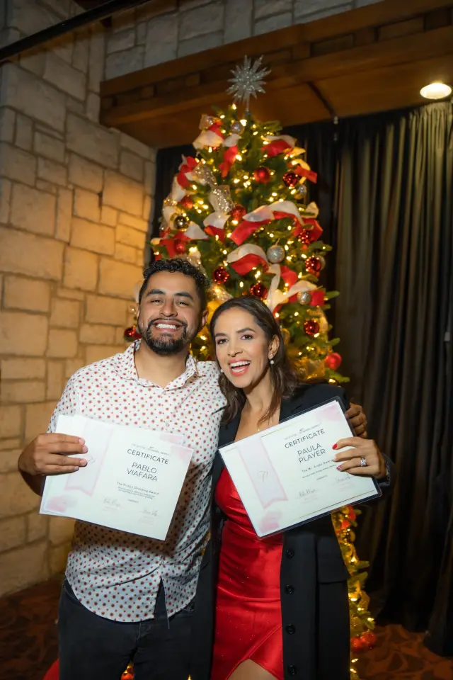 Two colleagues holding up certificates at a holiday party