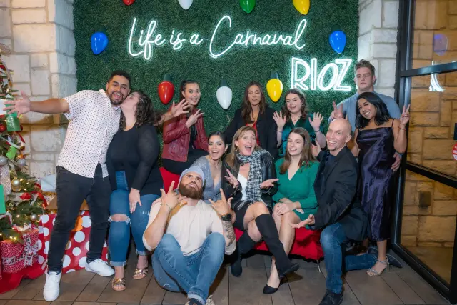 Party guests posing in front of a neon sign on a greenery wall