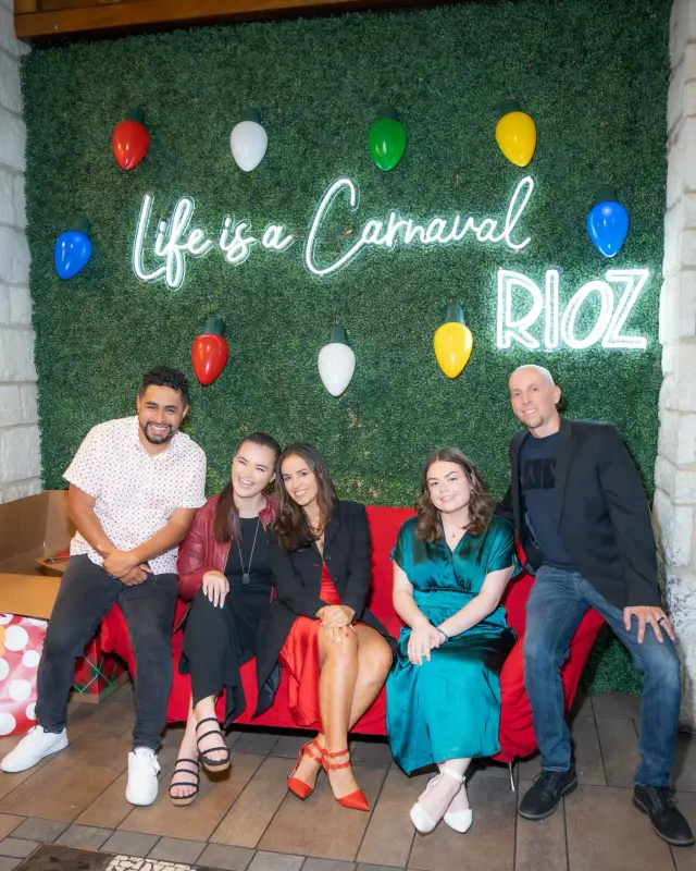 Group sitting on a red sofa in front of a greenery wall with a neon sign