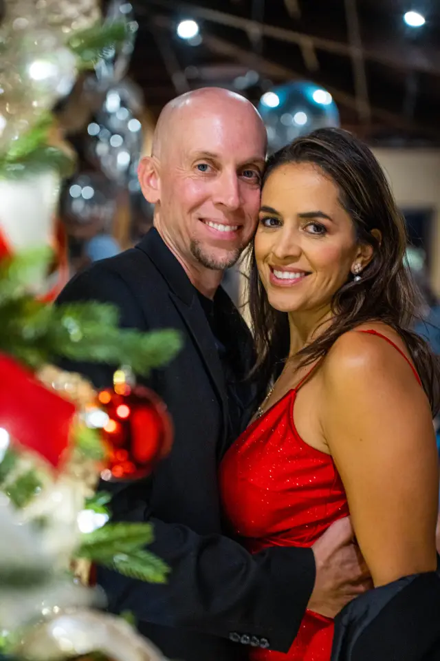 Couple smiling by a Christmas tree at a holiday party