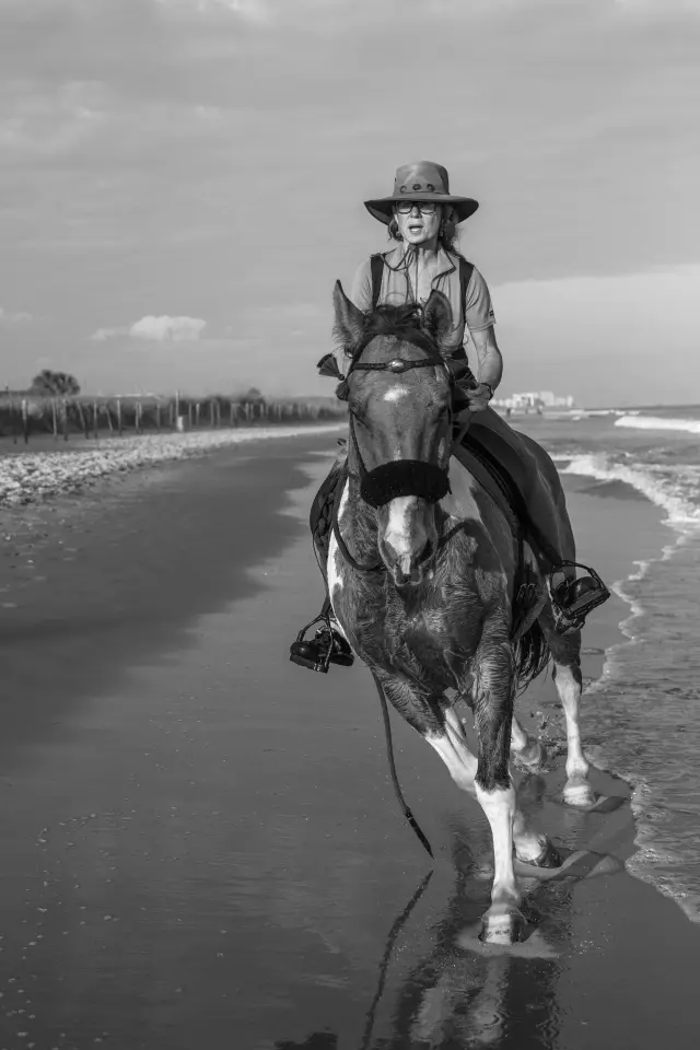 Black and white photo of a rider in a cowboy hat on horseback at the water's edge