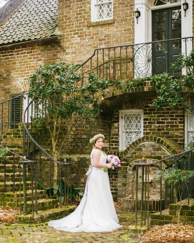 Bride standing at the foot of a brick staircase with iron railings and ivy