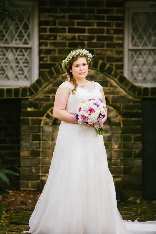 Bride with a flower crown and bouquet in front of a brick wall with arched windows