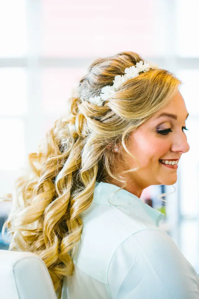 Smiling bride with long curled blonde hair and a flower crown, looking over her shoulder