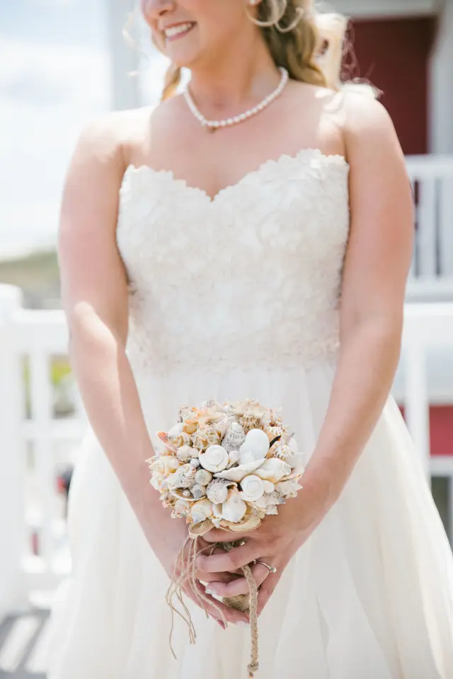 Bride in a strapless lace gown holding a seashell bouquet