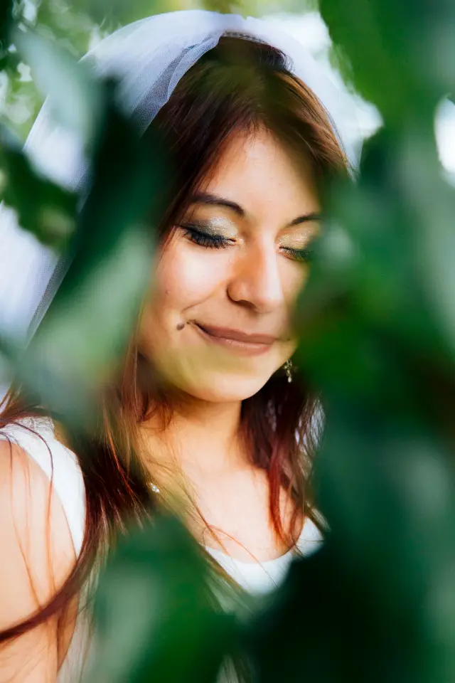 Bride smiling with her eyes closed, framed by green leaves