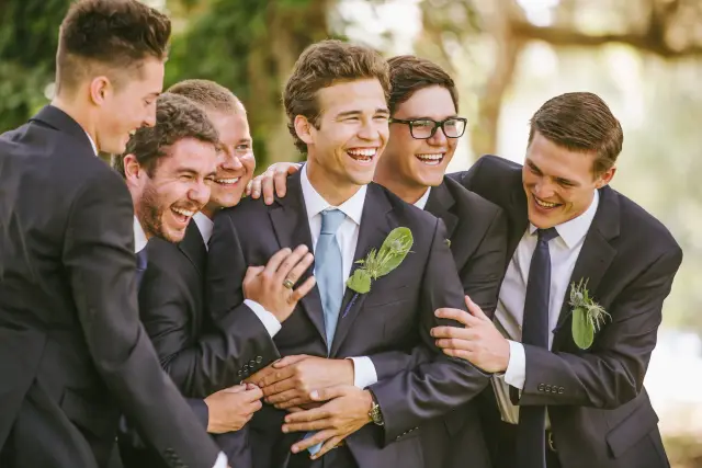 Groom laughing with his groomsmen in navy suits, arms around each other