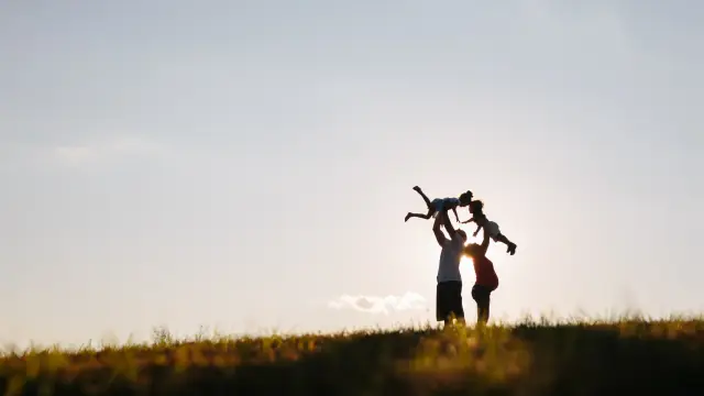 Silhouette of a parent lifting a child into the air at sunset