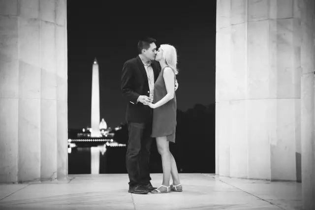 Black and white photo of a couple kissing at the Lincoln Memorial with the Washington Monument behind them