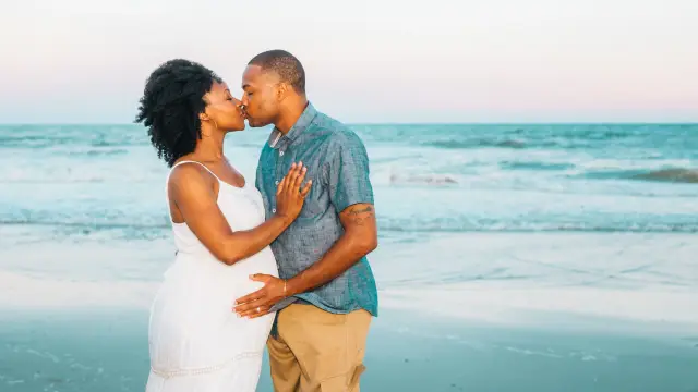 Couple kissing at the water's edge, she in a white dress, he in a blue shirt