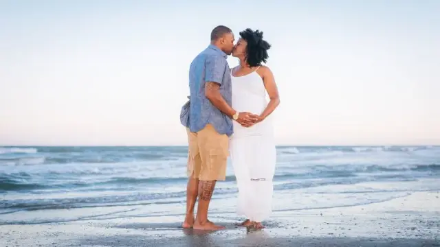 Couple kissing on the beach with the waves behind them