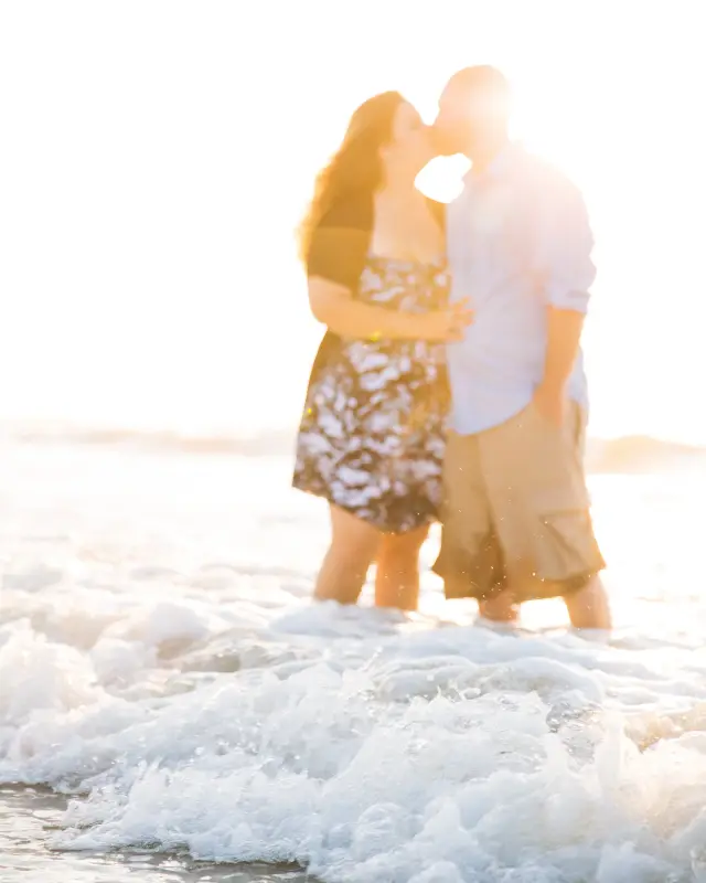 Couple kissing in the surf, backlit by the sun