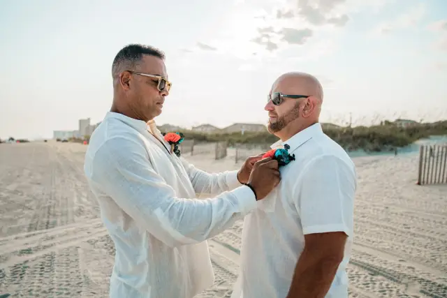 Groomsman pinning a boutonniere on the groom on the beach before the ceremony