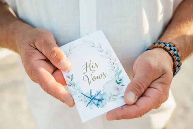 Groom holding a card titled His Vows, painted with blue seashells