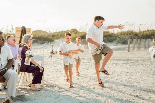 Ring bearer dancing up the aisle on the sand while the guests laugh
