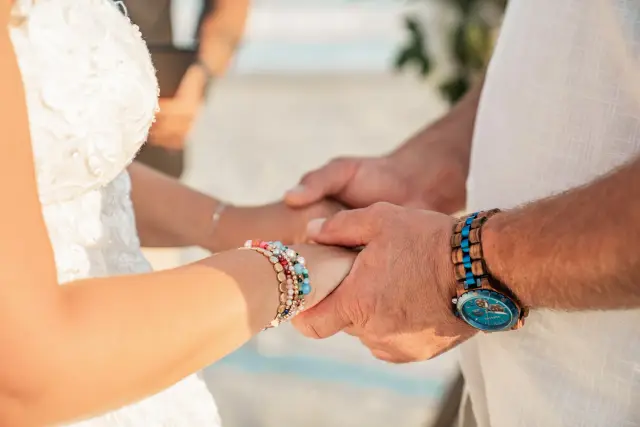 Bride and groom holding hands at the ceremony, close on their wrists and bracelets