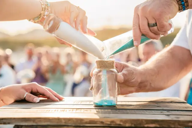 Bride and groom pouring blue and white sand into a jar during a beach sand ceremony