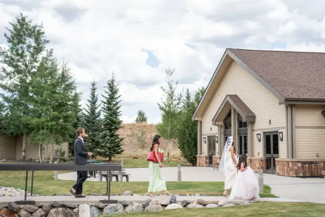 Bride and her bridesmaid walking across the lawn to the church as the groom waits