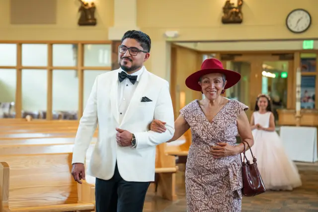 Groom in a white dinner jacket walking his mother down the church aisle
