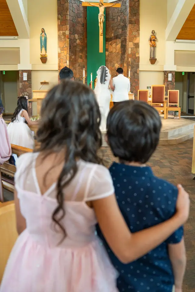 Flower girl and ring bearer arm in arm watching the ceremony from the back of the church