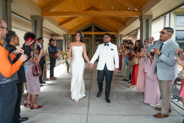 Newlyweds walking out of the church hand in hand as guests clap along the covered walkway