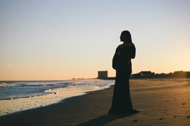 Silhouette of a pregnant woman at the water's edge at dusk