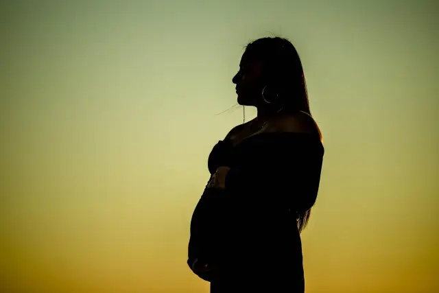 Silhouette of a pregnant woman against a golden evening sky