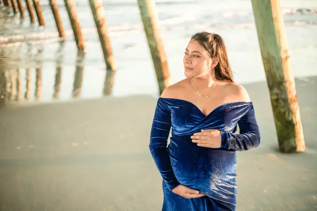 Mother-to-be in blue velvet standing among the pilings under the pier