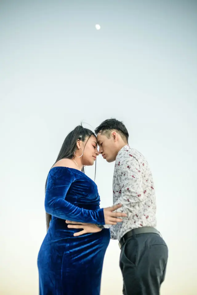 Expecting couple touching foreheads on the beach under a clear evening sky