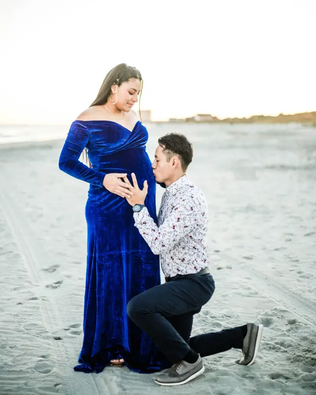 Partner kneeling in the sand to kiss the baby bump