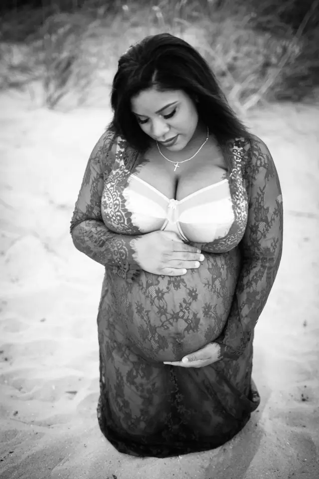 Black and white photo of a mother-to-be in a lace robe kneeling in the dunes