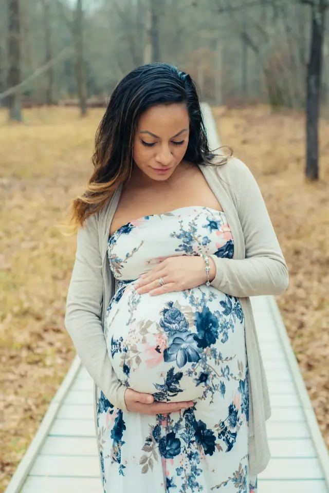 Mother-to-be in a blue floral dress and cardigan on a wooden boardwalk through the woods