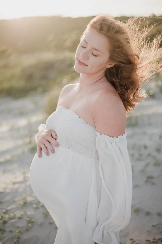 Mother-to-be in white with her eyes closed and the wind in her hair at golden hour
