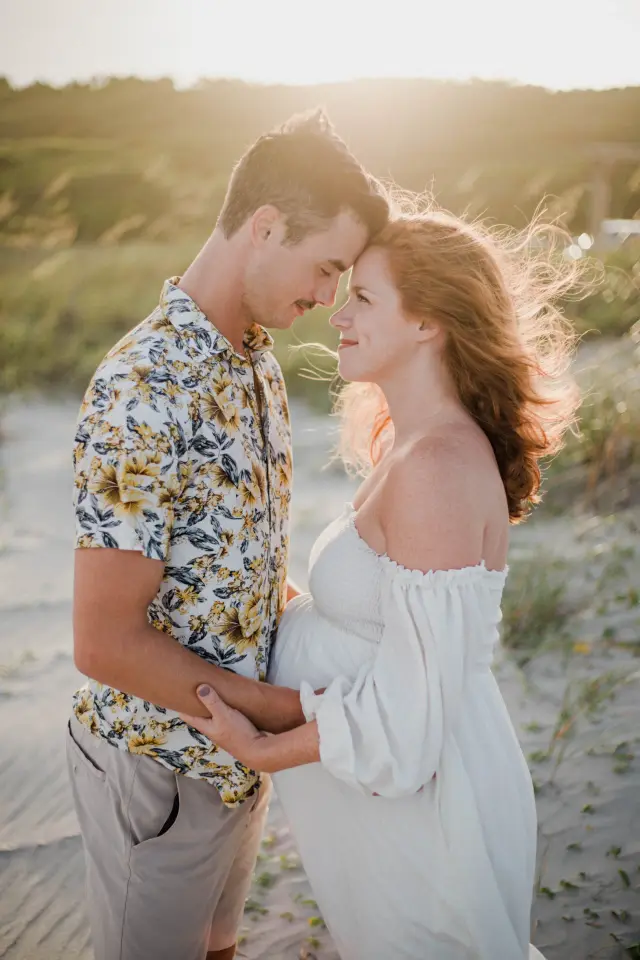 Expecting couple touching foreheads in the dunes at golden hour