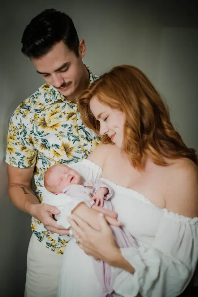 New dad and mom holding their sleeping newborn by the window