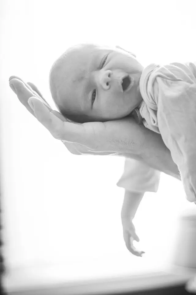 Black and white photo of a newborn yawning in a parent's hand